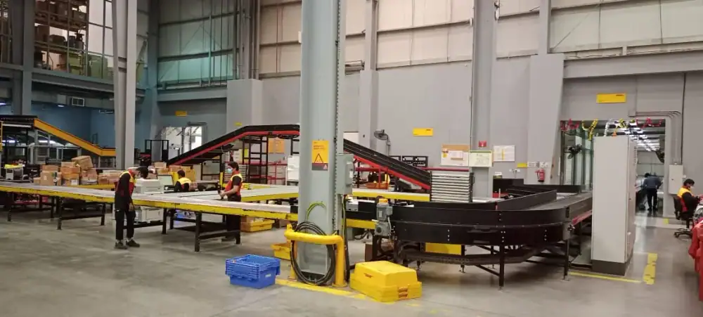 Staff sorting parcels at yellow workstations beside curved belt conveyors in the DHL distribution center, Jeddah, Saudi Arabia