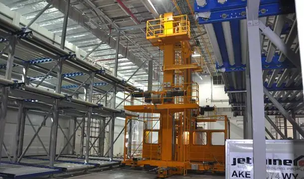 Yellow elevating transfer vehicle beside multi-level ULD storage racks at Muscat International Cargo Terminal, Oman